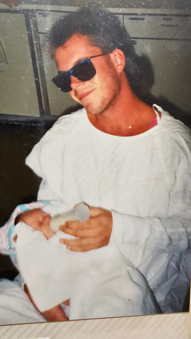 A family photograph of a man holding a newborn baby